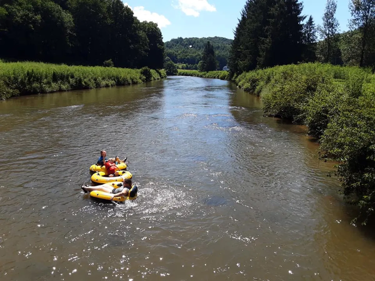 A lively scene of people in colorful inflatable tubes floating down the river, surrounded by lush greenery and a bright, inviting atmosphere. The river is calm and the setting feels playful and adventurous, perfect for summer fun.