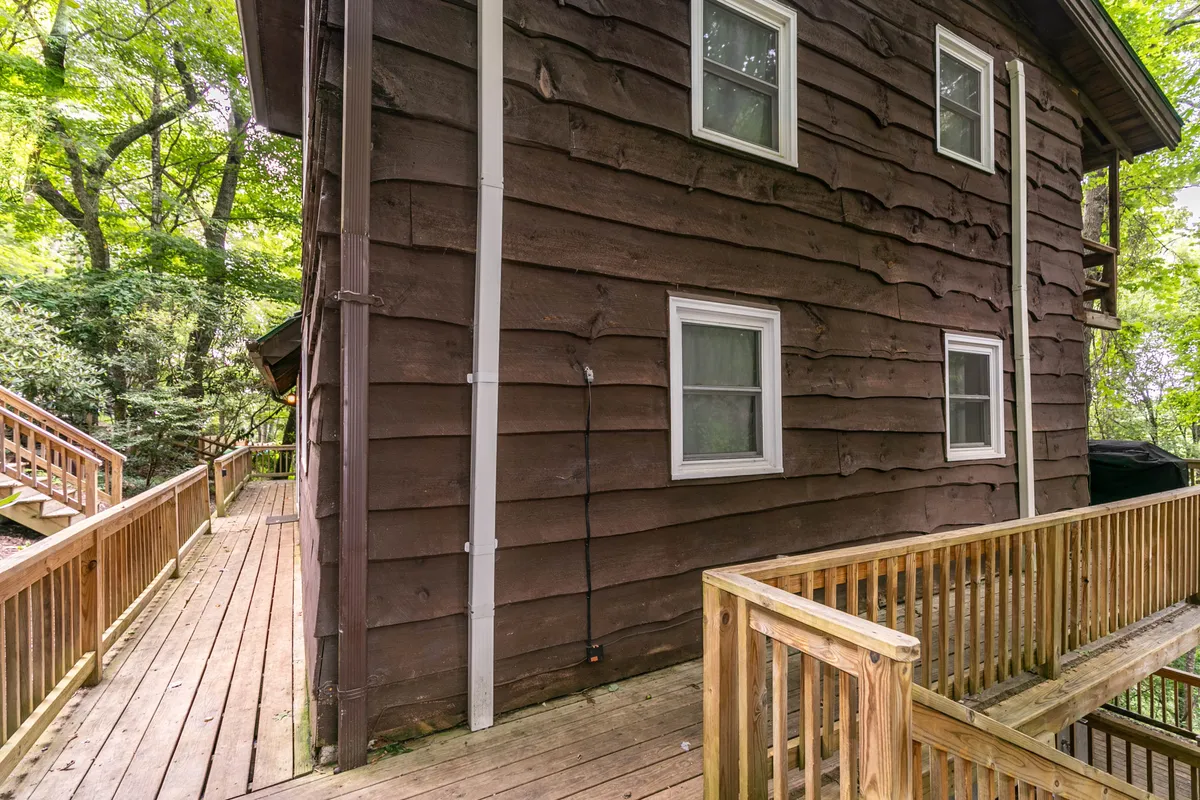 A tranquil exterior shot of the cabin, showing the wooden siding and deck nestled among mature trees. The inviting deck offers a spot to watch for wildlife, while the forested surroundings evoke the sense of adventure and proximity to trails for walking and exploring with pets.