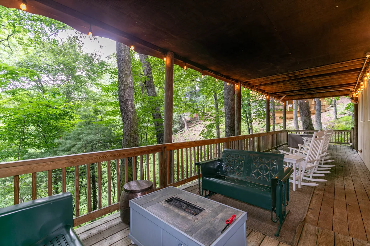 Featuring a welcoming wooden deck with a cozy fire pit, green seating, and rocking chairs, this scene is surrounded by greenery. The area hints at intimate conversations and relaxing evenings under the stars.