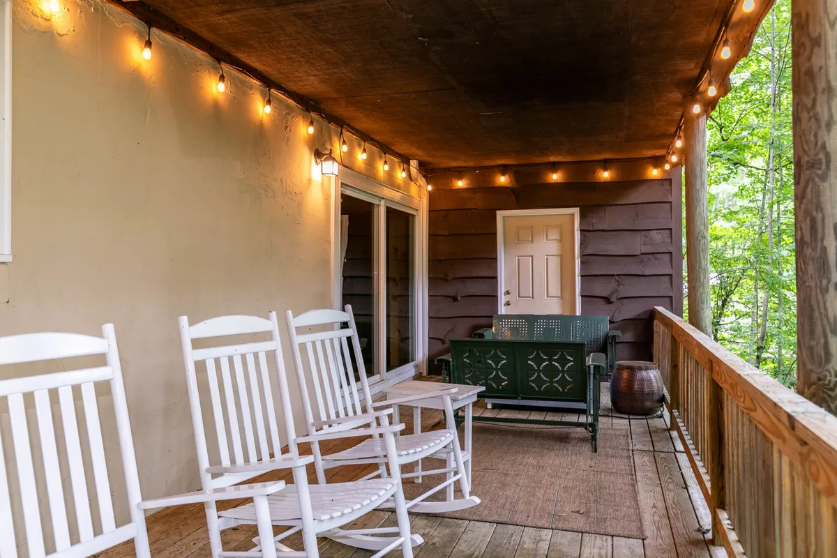 This image displays a deck with comfortable rocking chairs, an outdoor sofa, string lights, and a wooden railing overlooking the forest, creating a perfect setting for enjoying sunsets or quiet moments with nature.