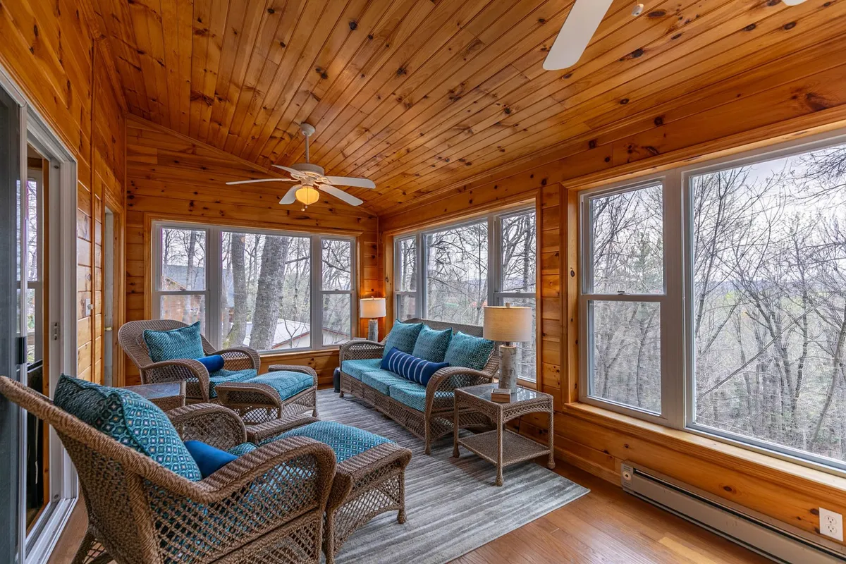 This image highlights a serene interior space filled with comfortable seating, a wooden ceiling, and expansive large windows that flood the room with natural light. The presence of decorative pillows and the tranquil mood evoke a perfect spot for reading, enjoying morning coffee, or soaking in the surrounding scenery.