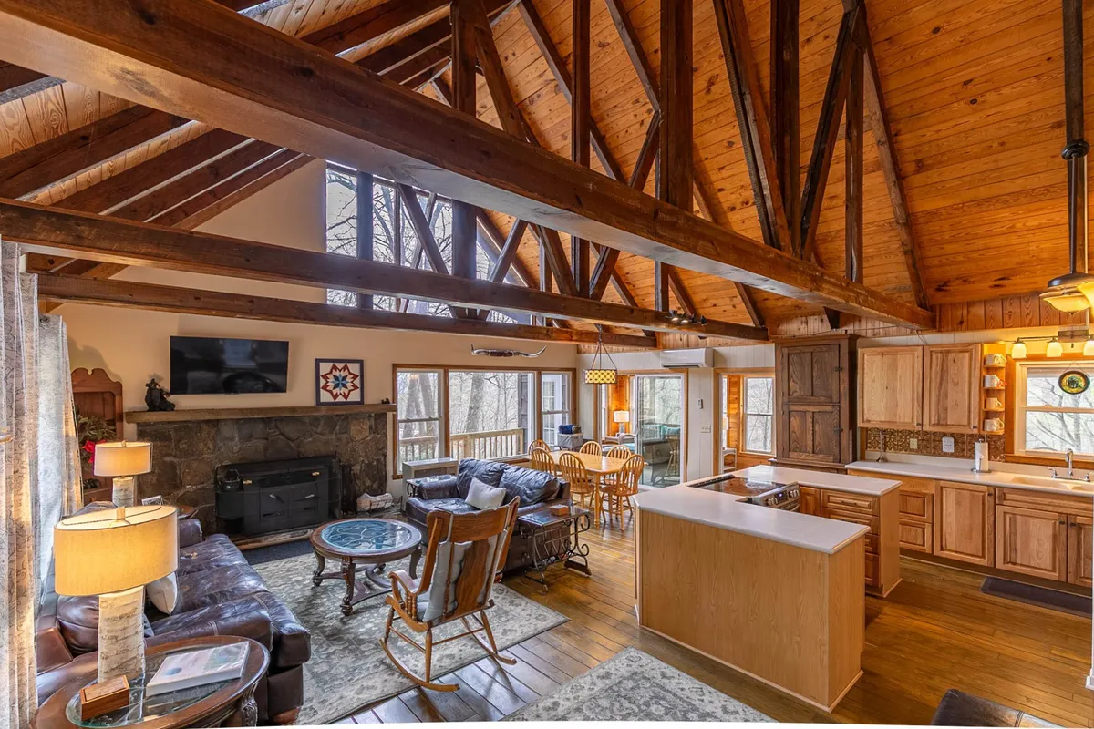 A warm and inviting setting featuring exposed wooden beams above, a stone fireplace at the center, and a comfortable seating area adjacent to a classic dining table. The harmonious layout encourages shared meals and cozy evenings by the fire, echoing the spirit of connection and celebration.