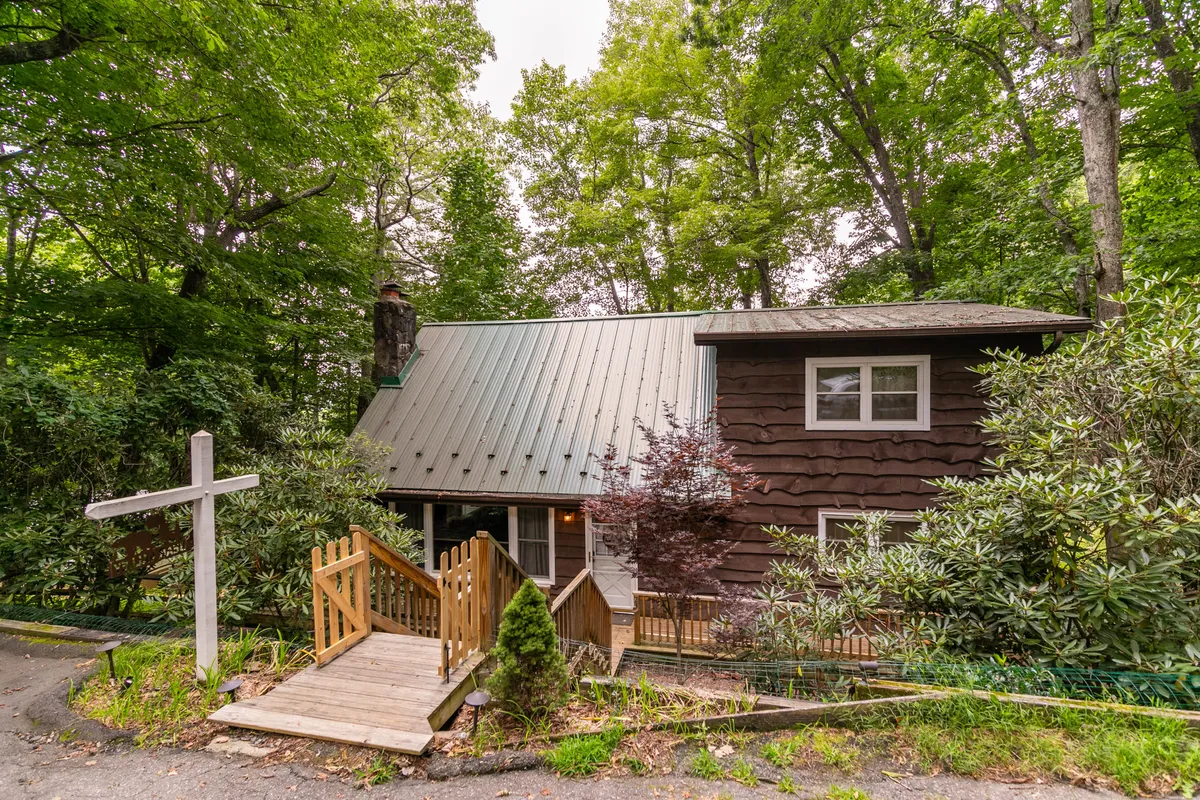 Wooden steps lead up to a distinctively designed house set amid vibrant greenery. The unique architecture and abundant trees highlight the sense of escape and immersion in the natural environment, while the steps and porch evoke arrival and welcome.