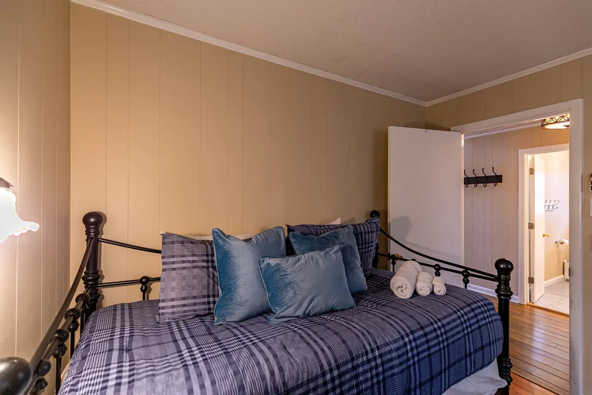 A loft-style sleeping space with a daybed outfitted in plaid bedding and blue accent pillows, set on wooden flooring. The design feels playful yet cozy, ideal for flexible sleeping arrangements or children and guests.