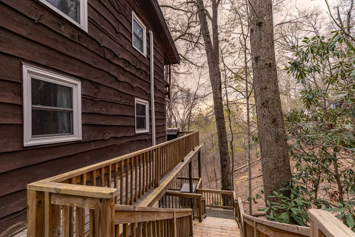 A peaceful view of the cabin's wooden deck surrounded by tall trees, with dappled sunlight filtering through the forest canopy. The deck provides an immediate connection to nature, inviting relaxation and outdoor enjoyment. The sightlines suggest easy access to nearby trails and the wooded landscape beyond.